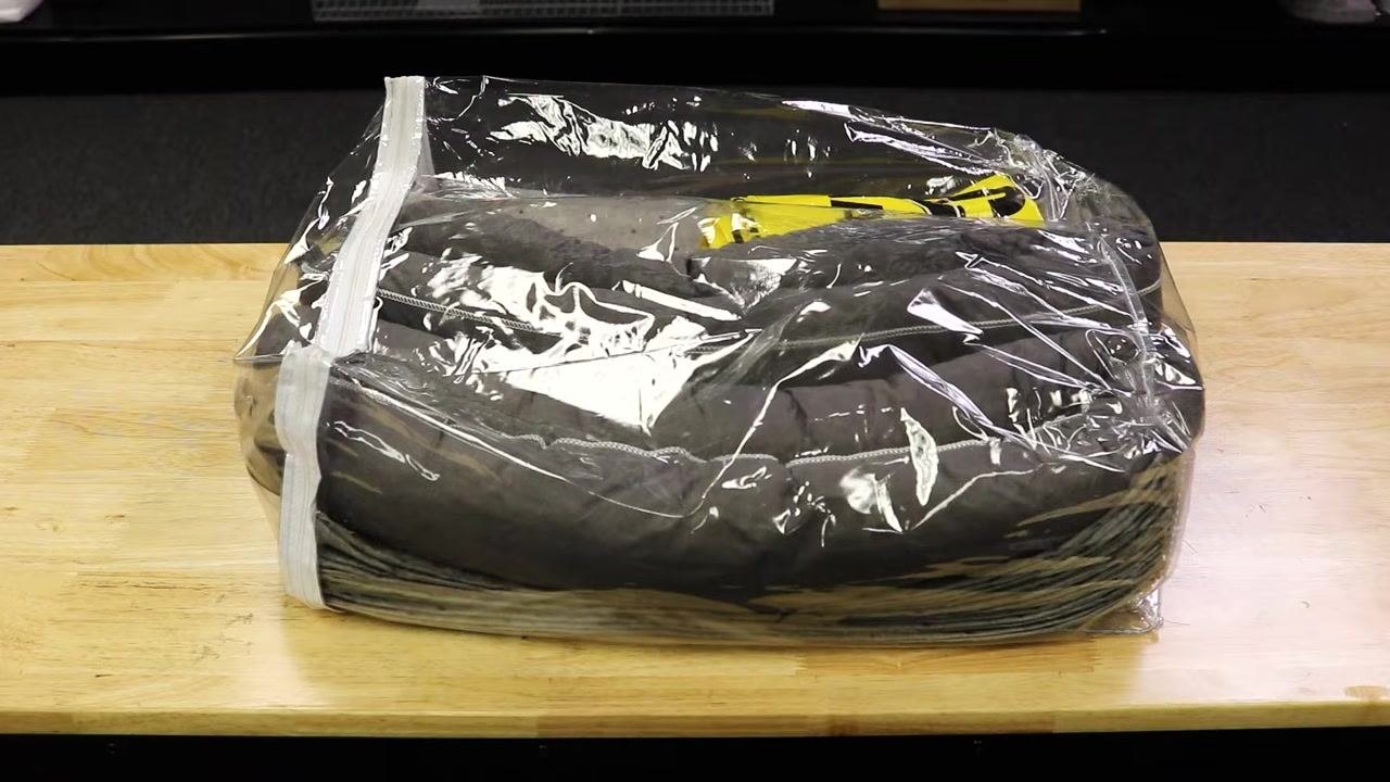 Spill kit supplies including cellulose-filled socks, absorbent pads, a yellow chemical-resistant container, and a clear plastic bag labeled "Tools Needed" on a wooden table