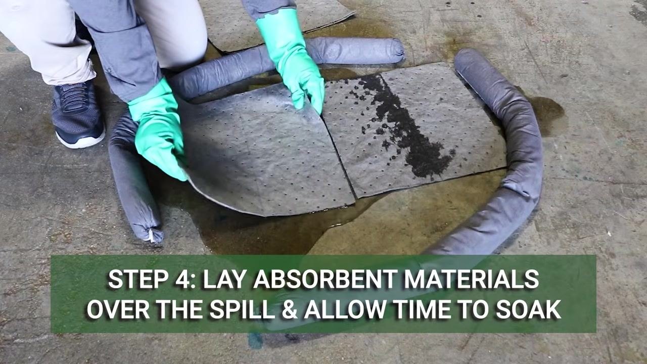 Person wearing chemical-resistant gloves placing absorbent pads over a contained spill, with on-screen text reading "Step 4: Lay absorbent materials over the spill and allow time to soak"