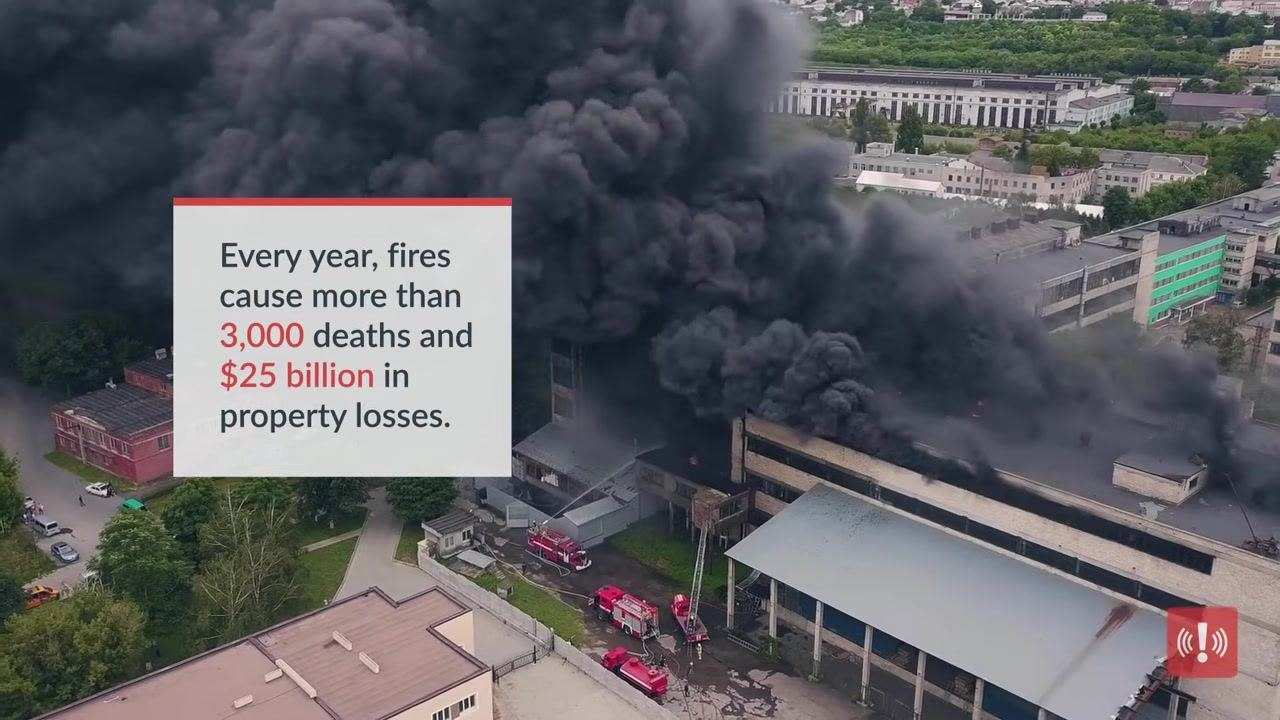 Aerial view of a large building fire with thick black smoke and fire trucks on scene, illustrating the scale of risk fires represent.