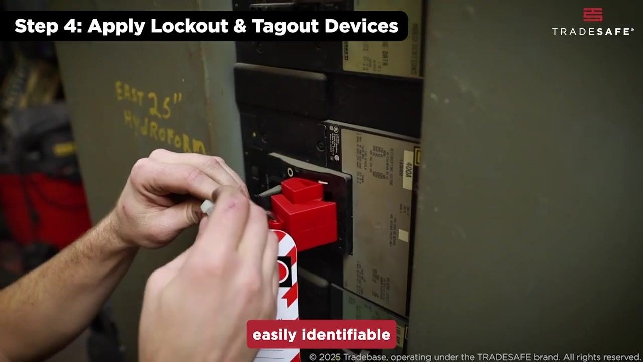A worker's hands attach a striped "DANGER" lockout tag to a red lockout device on an electrical panel.