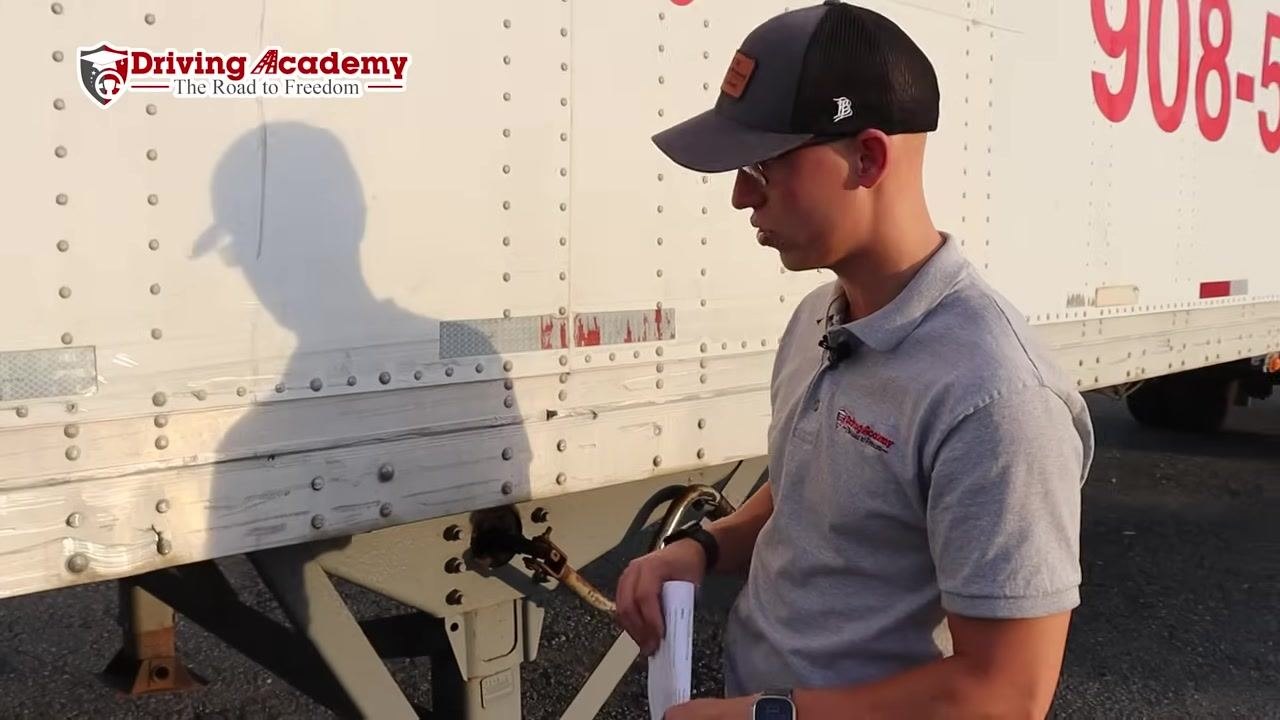 Instructor inspecting the area near the landing gear, with the trailer wall and landing gear visible.