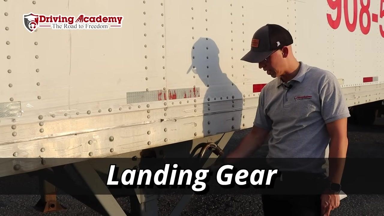 Instructor standing beside the trailer emphasizing thorough inspection of the landing gear.