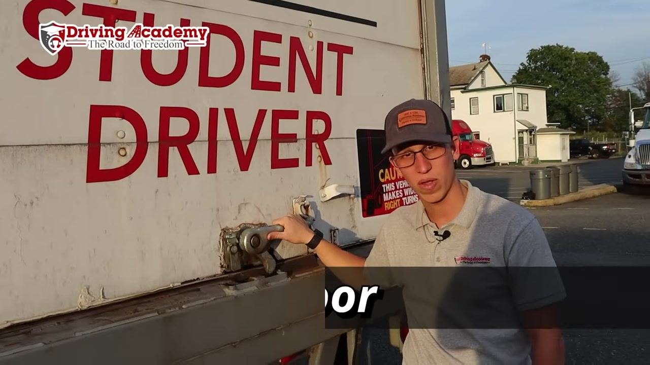 Instructor demonstrating the rear trailer door lock with a hand on the locking handle.