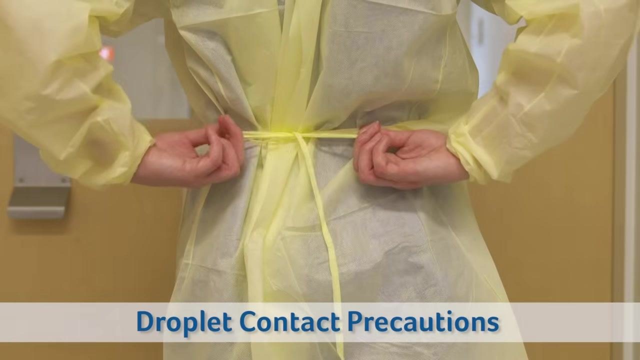 Healthcare worker in scrubs performing hand hygiene, rubbing hands together. Text overlay: "Droplet Contact Precautions"
