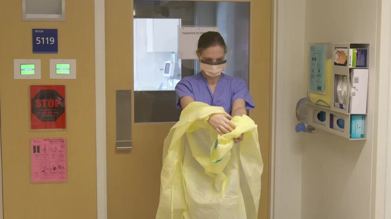 Healthcare worker in a yellow gown, untying at the neck as the first step of gown removal.