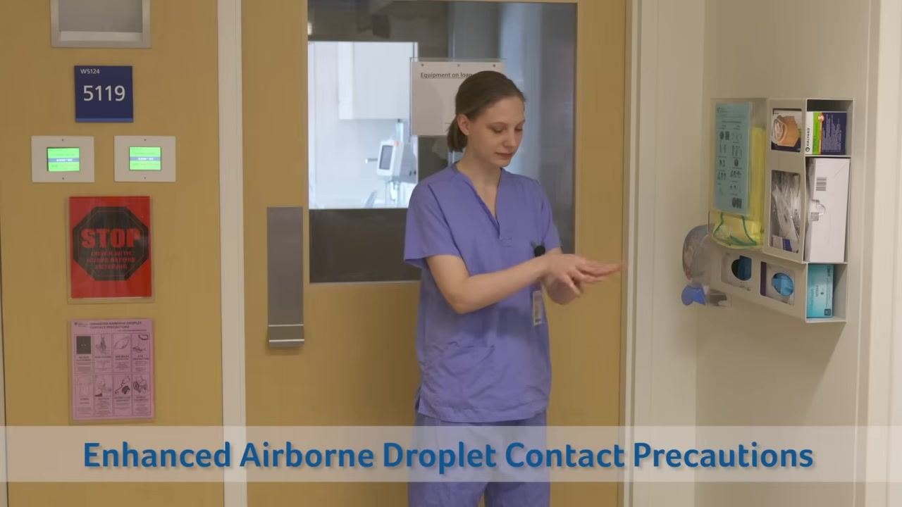 Healthcare worker in scrubs performing hand hygiene in front of a patient room door and PPE supply station. Text overlay: "Enhanced Airborne Droplet Contact Precautions"
