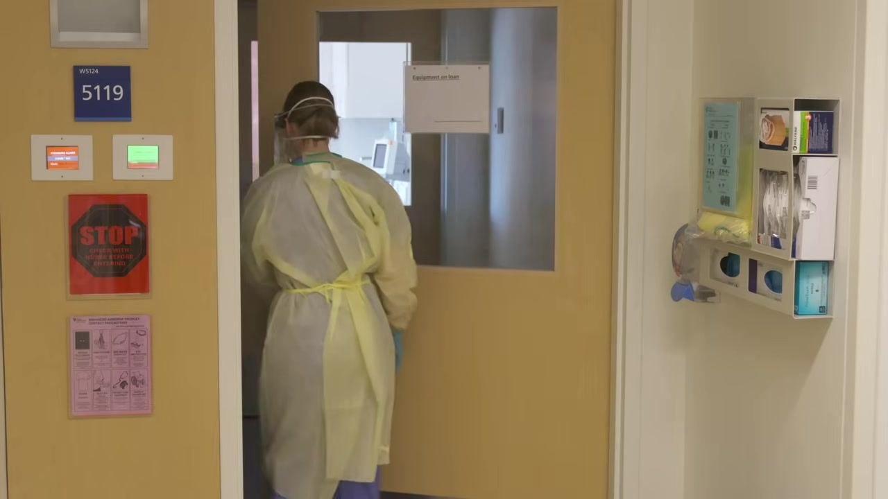 Healthcare worker in full PPE entering the negative pressure room, ensuring the door is closed behind.