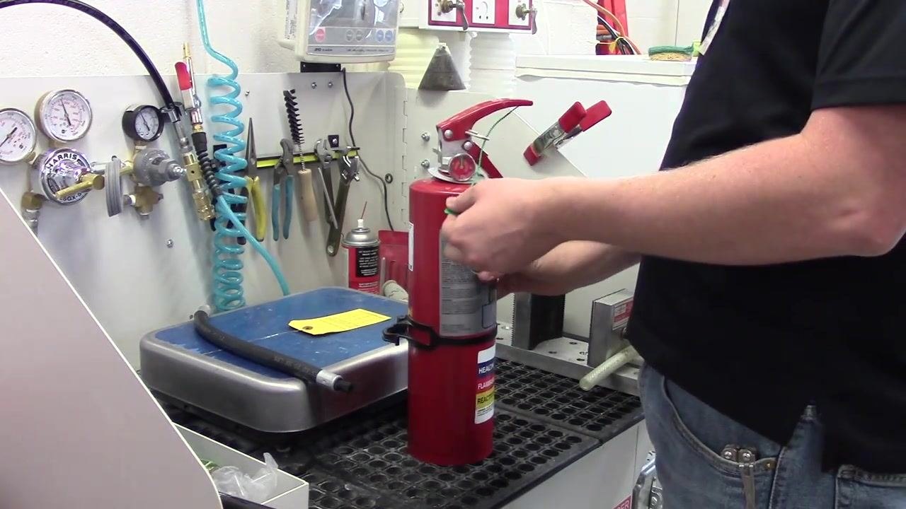 A person threading and securing a green zip tie through the pin and under the handle of the fire extinguisher.