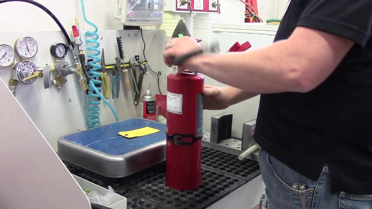 A person reattaching the hose to the fire extinguisher, twisting it by hand to ensure a proper fit.