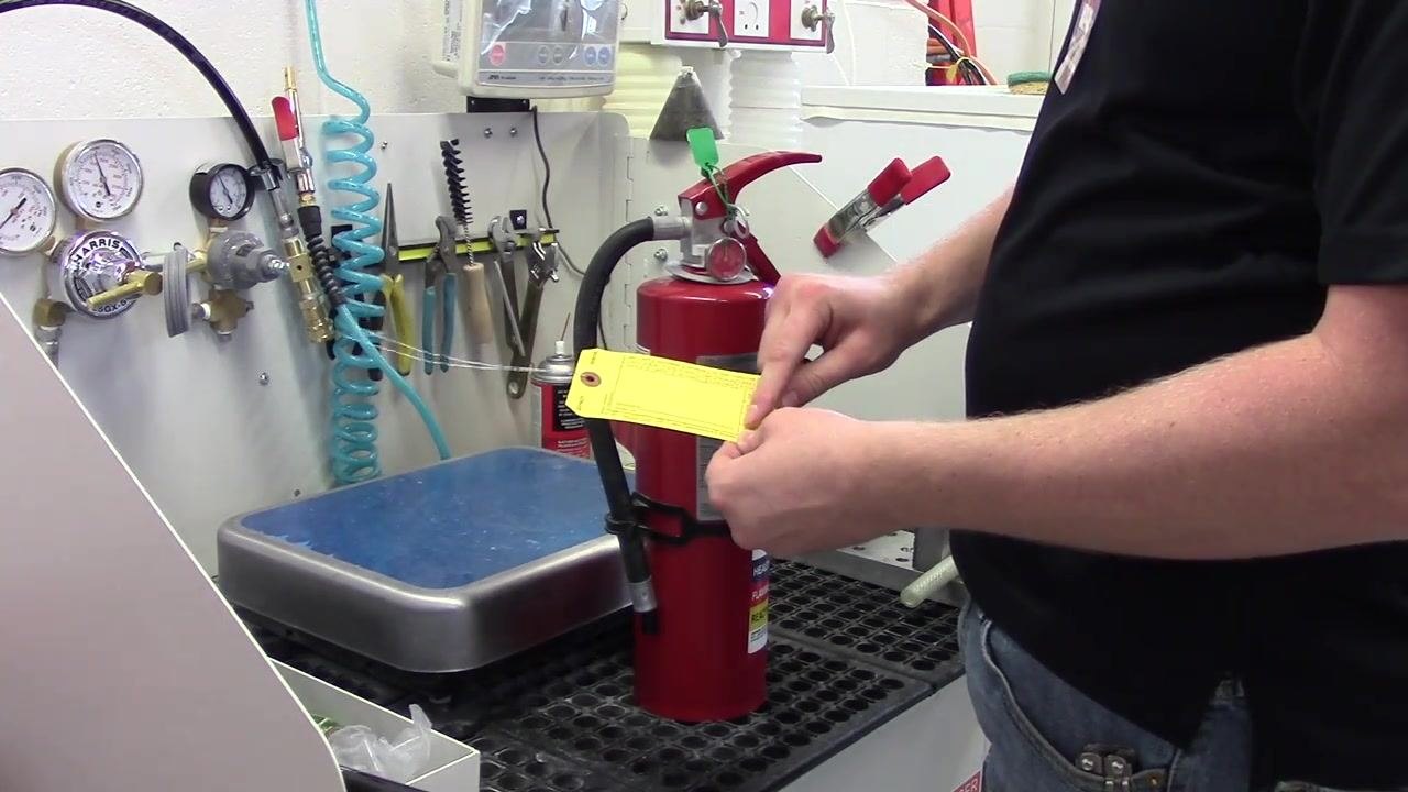 A person holding a new yellow inspection tag, preparing to punch and attach it to the fire extinguisher.
