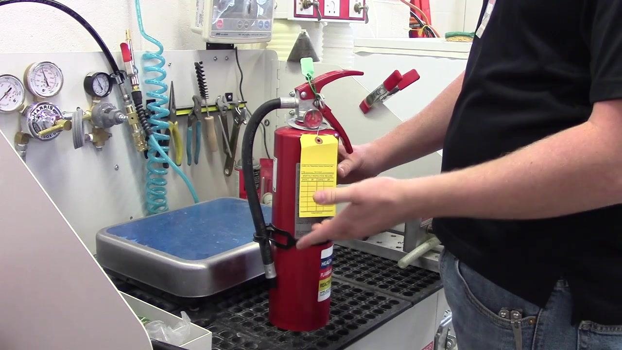 A person creasing and positioning the inspection tag so it sits flat and visible on the front of the fire extinguisher.