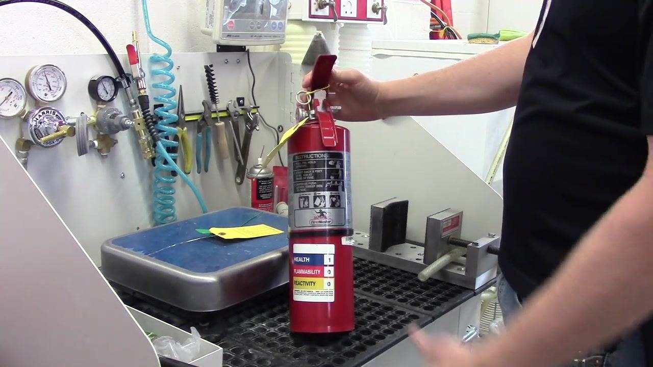 A person holding a fire extinguisher, showing the instruction and safety labels for inspection.
