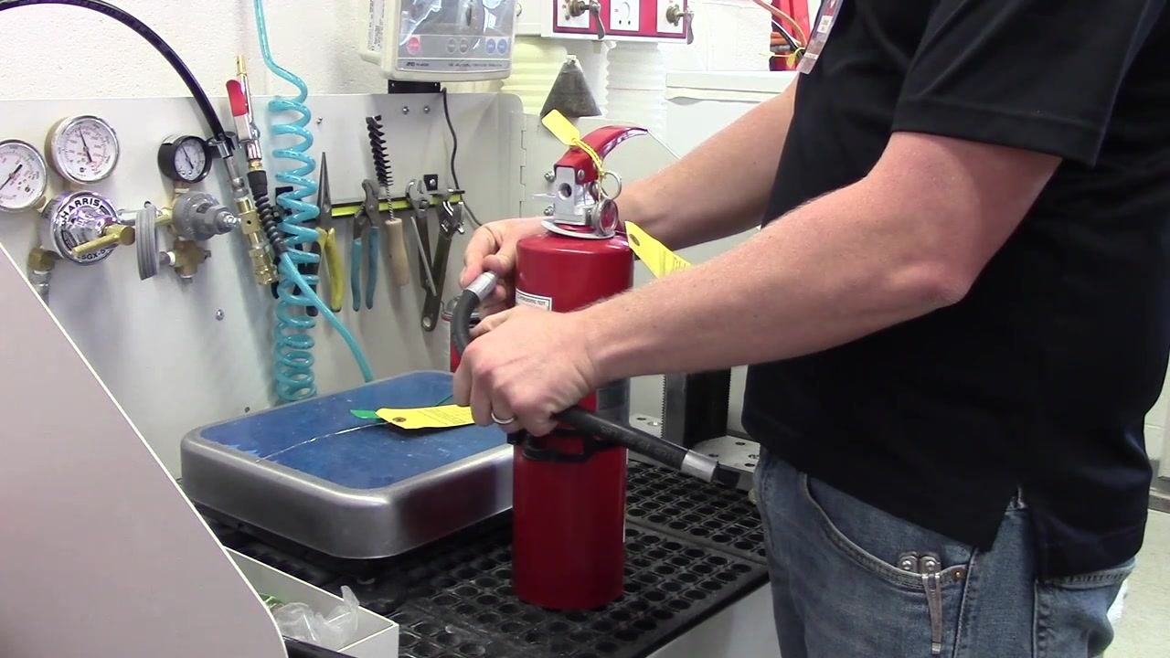 A person removing the hose from the fire extinguisher for inspection.