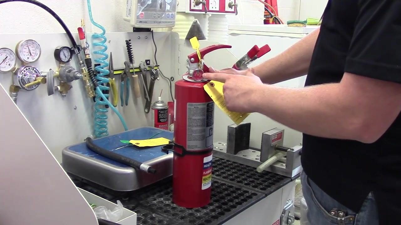 A person pointing to the pressure gauge on the fire extinguisher, confirming the needle is in the green zone.