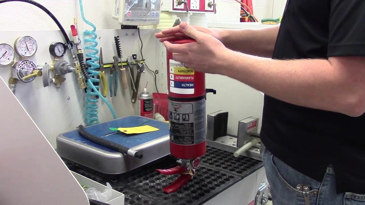 A person holding the fire extinguisher upside down, performing the fluffing procedure to loosen the internal agent.