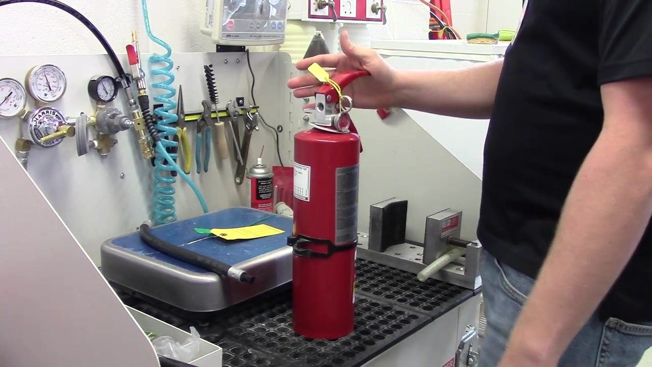 A person returning the fire extinguisher to an upright position after fluffing, preparing for the next maintenance step.