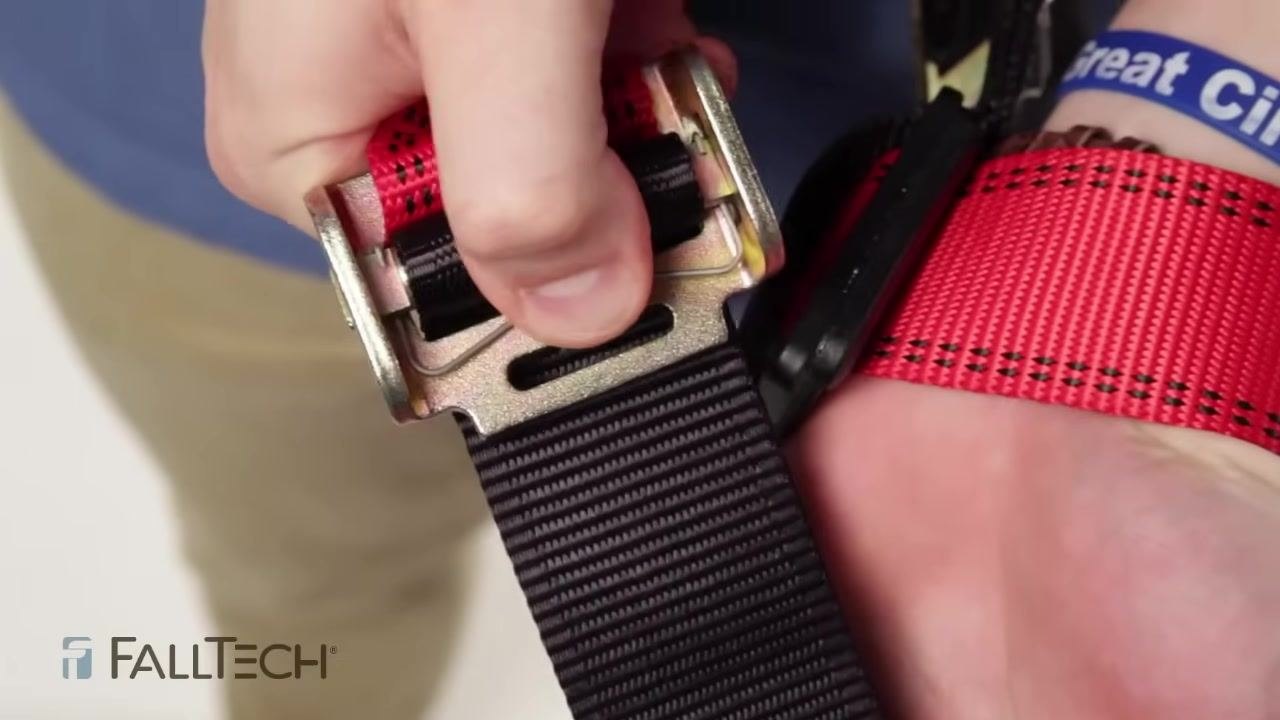 Close-up of a hand checking a harness buckle with a roller, confirming the roller spins freely and the webbing passes through the adjuster