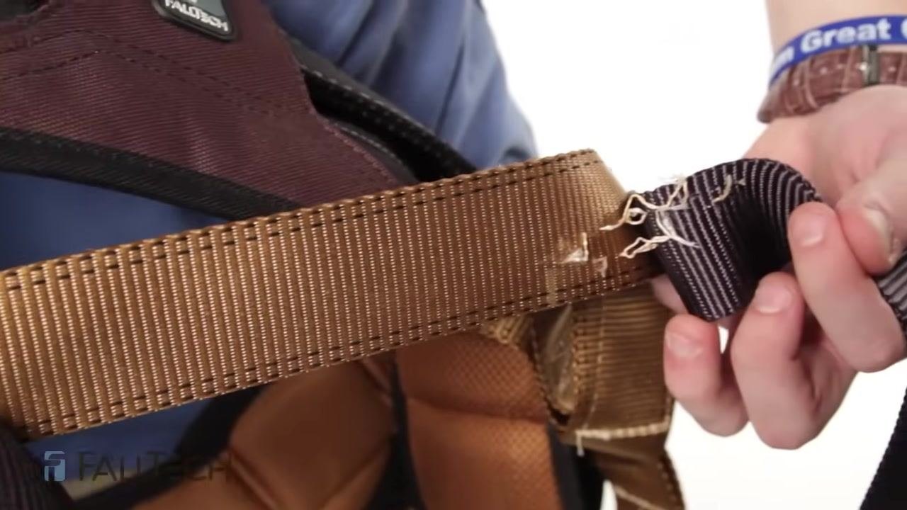 Close-up of red harness webbing showing intact stitching against a blue FallTech shirt, highlighting the importance of checking for loose or missing stitches