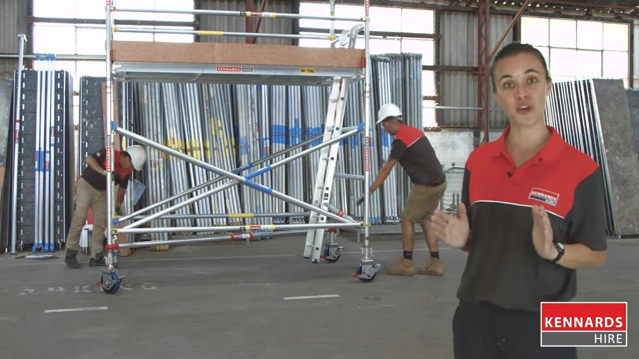 Two workers performing final checks on the scaffold, one adjusting a base component and one checking a vertical post