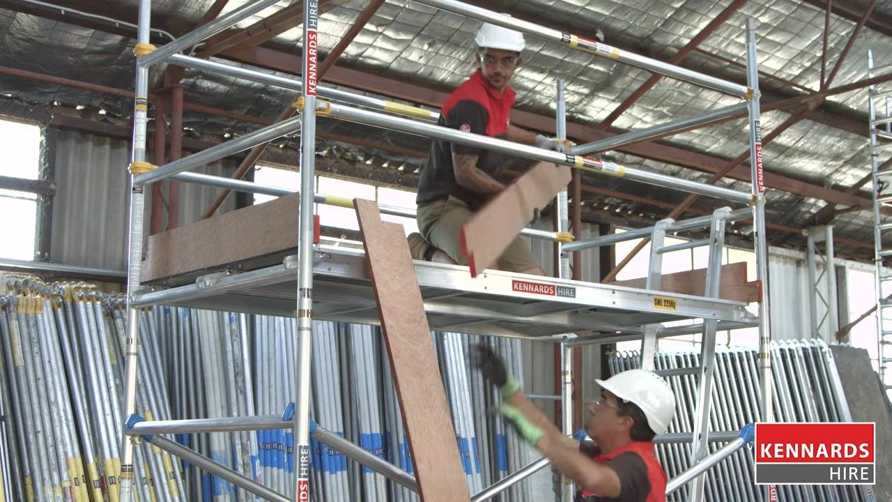 Worker installing wooden toe boards on the upper platform while another worker hands up a board