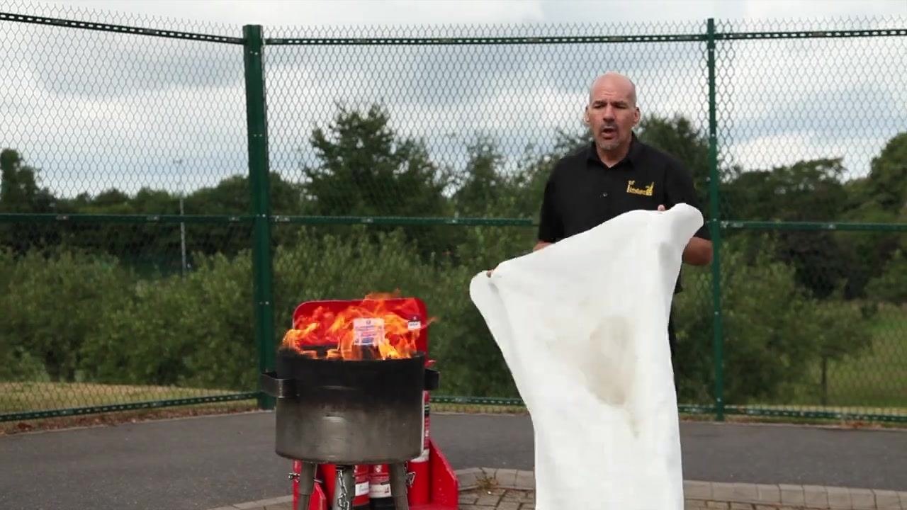 Person standing near a fire with a fire blanket placed over the flames.