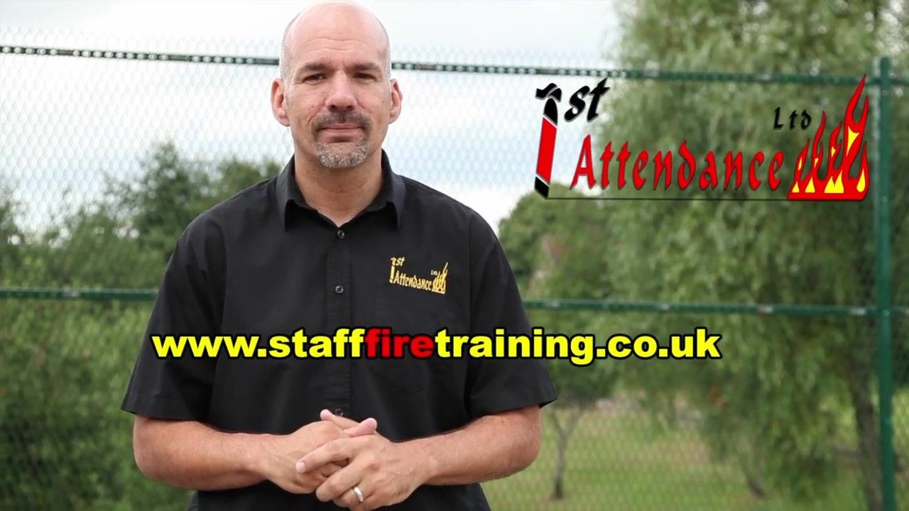 Instructor standing outdoors, with the First Attendance Ltd logo and website (www.stafffiretraining.co.uk) prominently displayed on the screen.