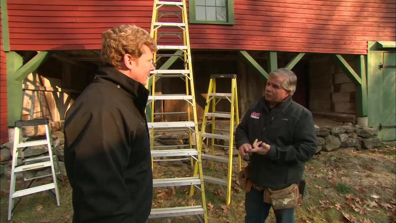 Several ladders made of wood, fiberglass, and aluminum are displayed outside a red and green building while two people discuss ladder safety.