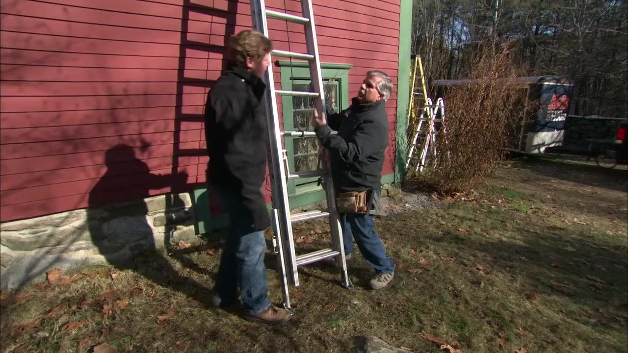A person stands to the side of the upright ladder, preparing to extend the upper section.