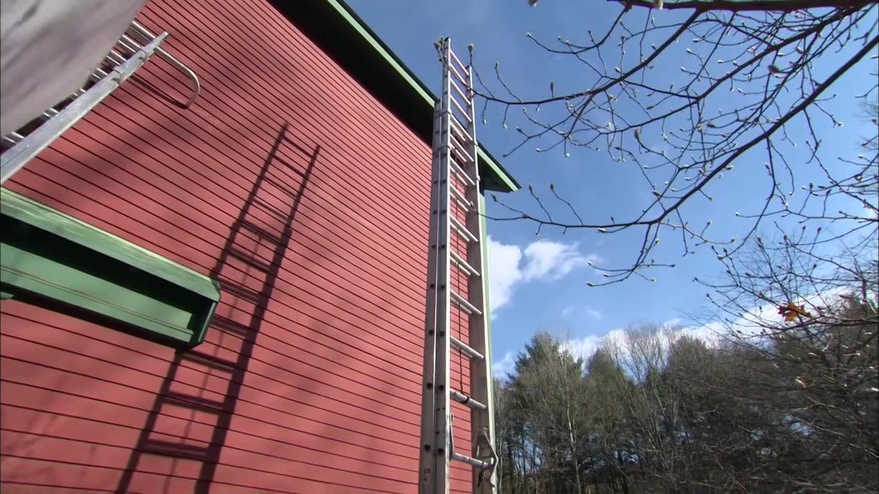A close-up of a hand gripping a rung and pushing the upper section of the extension ladder upward.