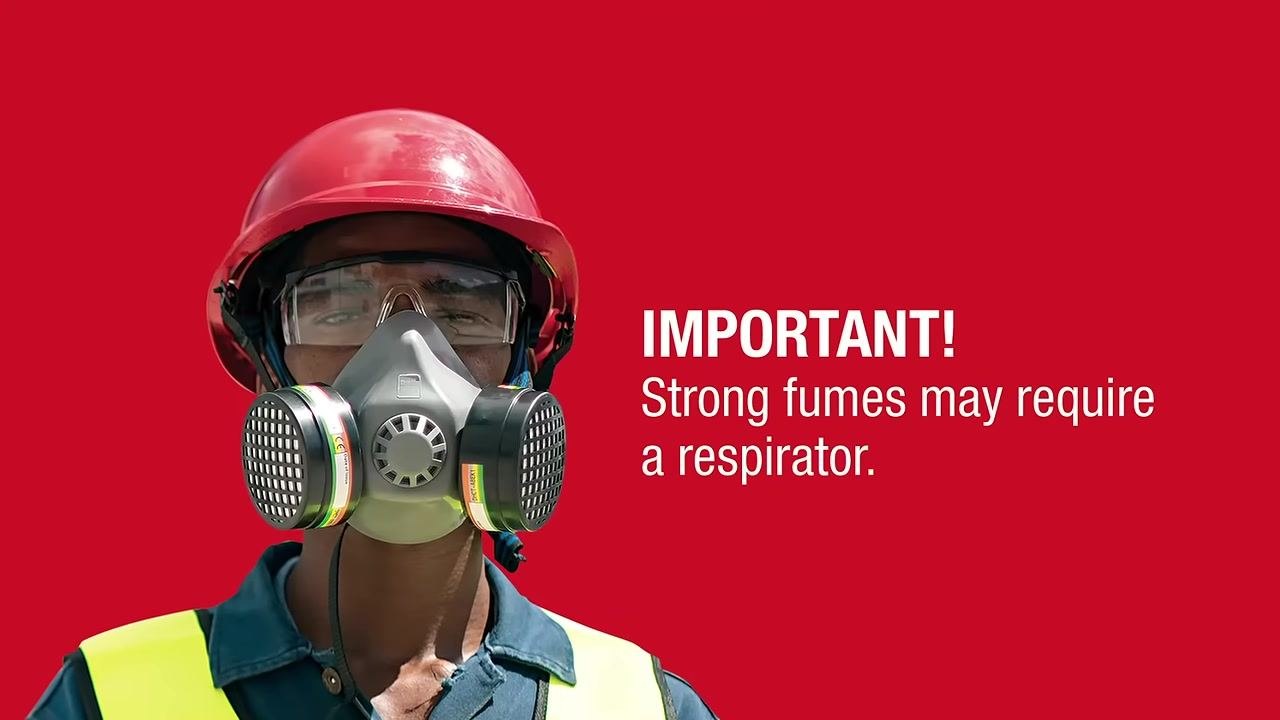 Person wearing a high-visibility vest labeled "SPILL" donning a dust mask while preparing PPE outdoors near a building.