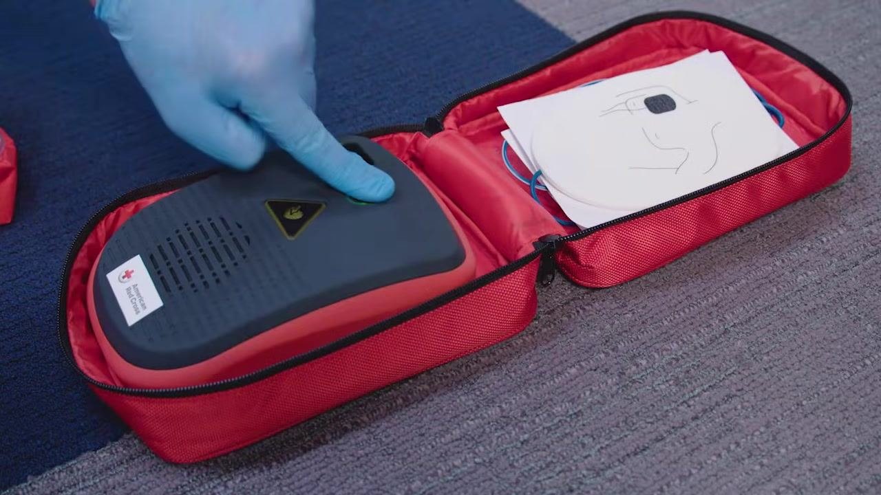 Two instructors, one holding a red AED case labeled "AED Trainer"