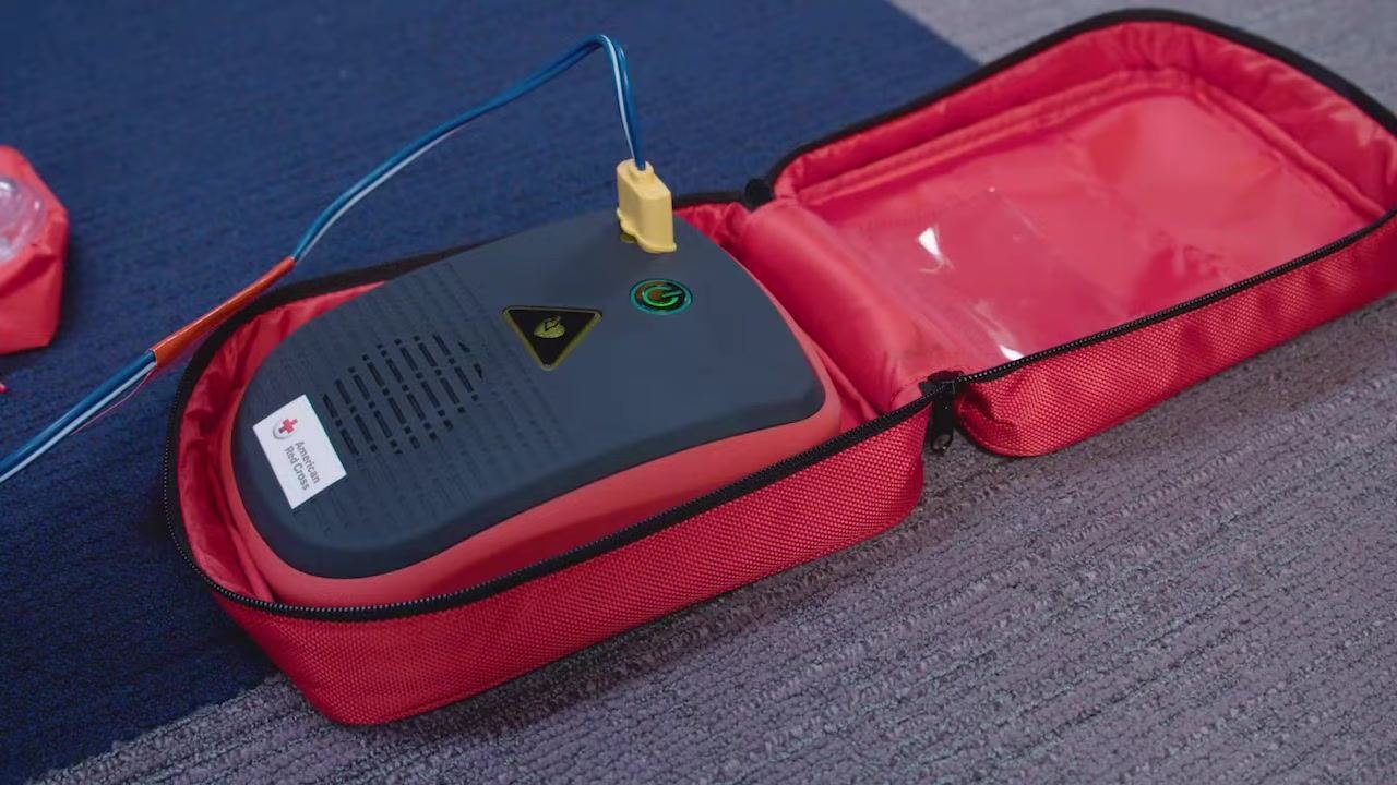 AED device in a red case with the pad connector cable plugged in, American Red Cross label visible