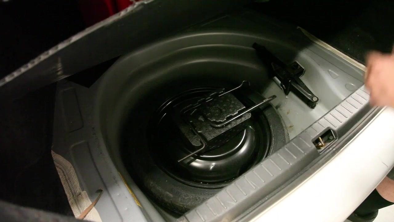 A digital tire inflator is used to check and inflate the spare tire in the trunk. The gauge reads 89.5 PSI, indicating the tire is being filled.