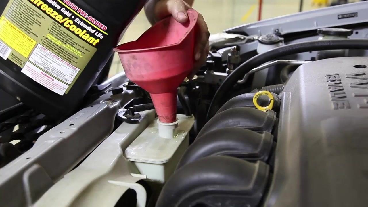 A close-up view of a drive belt inside the engine bay, illuminated by a flashlight. The belt is being visually inspected for cracks or tears.
