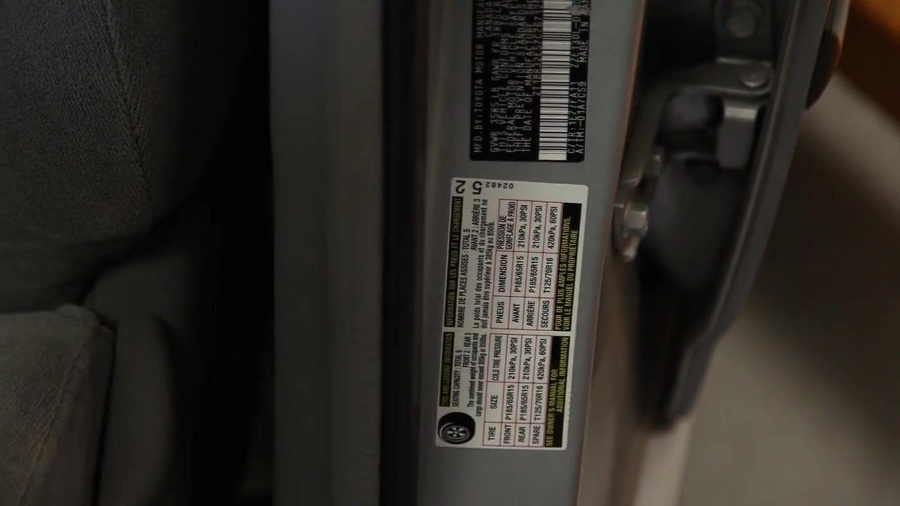 A close-up of the tire information sticker on the driver's side door jamb. A finger points to the sticker, which lists recommended tire pressures and tire sizes.