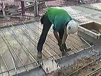 Worker observing and taking notes on a clipboard while another worker handles rebar at a construction site.