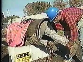Worker in a blue hard hat and denim jacket standing in front of a block wall, with on-screen text reading **"STEP 2 LIST HAZARDS."**