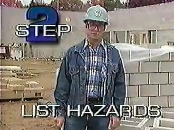 Worker in a white hard hat kneeling with a clipboard, taking notes while talking with another worker.