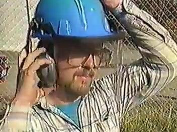 Worker adjusting hearing protection near a chain-link fence, illustrating a hazard introduced by the site environment.