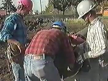 Three workers in hard hats and plaid shirts working together at the entrance of a large pipe, demonstrating teamwork and hazard awareness.