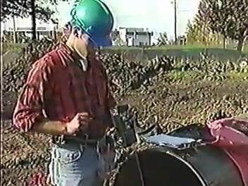 Worker in a green hard hat and gloves placing a wooden board into a large pipe to allow safer confined-space entry.