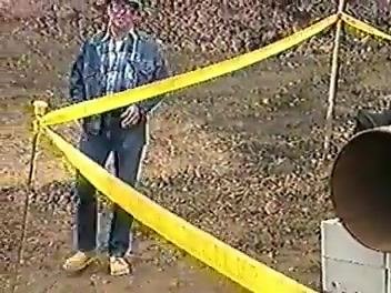 Worker in PPE standing behind yellow caution tape near the pipe, highlighting restricted access and hazard awareness.