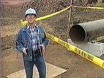 Worker in a blue hard hat standing in a taped-off construction area next to the pipe.