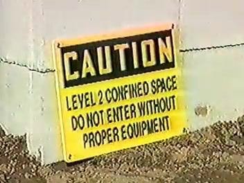 A yellow caution sign reading "LEVEL 2 CONFINED SPACE DO NOT ENTER WITHOUT PROPER EQUIPMENT," posted on a wall at a construction site.