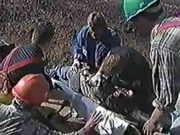 Several workers and responders attending to an injured person on the ground, using a stretcher and PPE.
