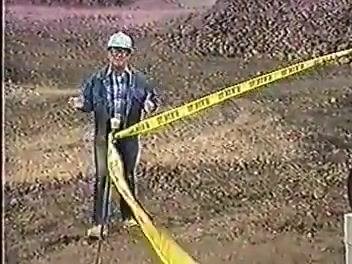 A worker in a hard hat stands behind yellow caution tape at a construction site, demonstrating hazard marking.