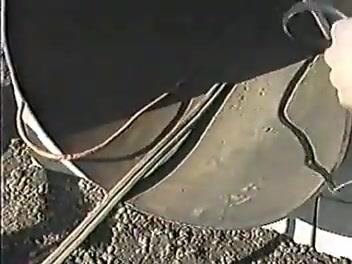 Close-up of the pipe entrance with an oxygen hose and grinding equipment visible; a worker's gloved hand holds equipment at the pipe opening.