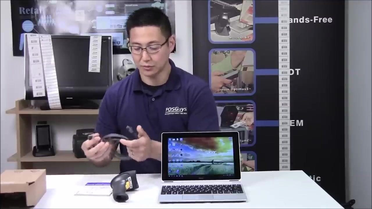 A person holding a USB cable and preparing to connect it to the barcode scanner, with the scanner, laptop, and quick start guide on the table.