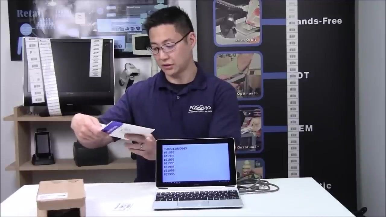 A person looking at the quick start guide, preparing to scan a configuration barcode, with the laptop and scanner on the table.