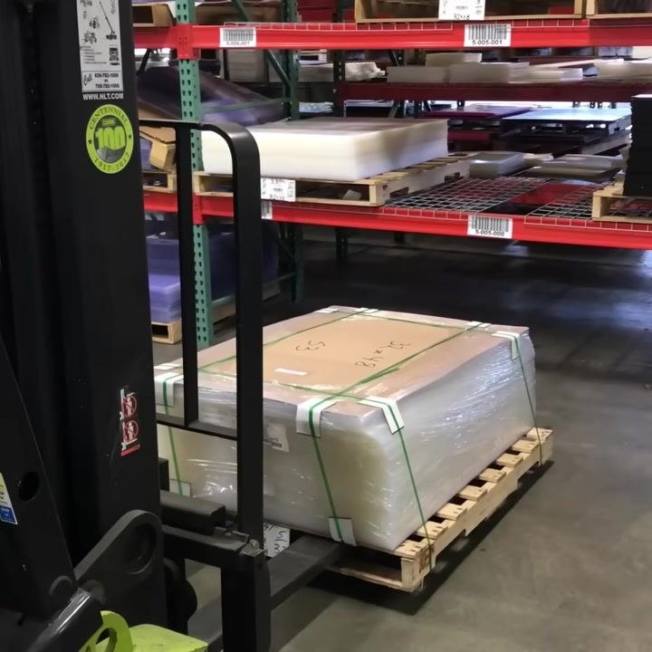 Forklift forks with pallet nearly on the floor, close-up of load and racking, warehouse shelving visible.